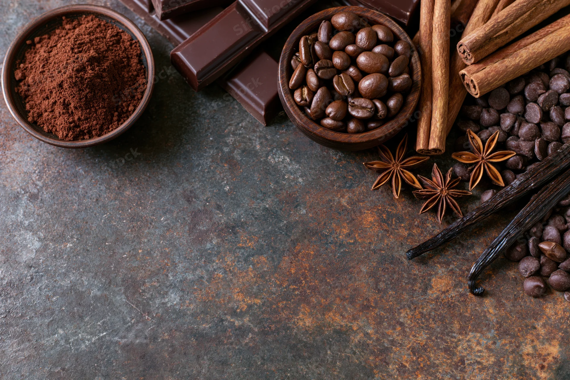 Chocolate bars, cocoa powder, coffee beans, cinnamon sticks, vanilla pods, and star anise arranged on a rusty metal surface in a flat lay composition