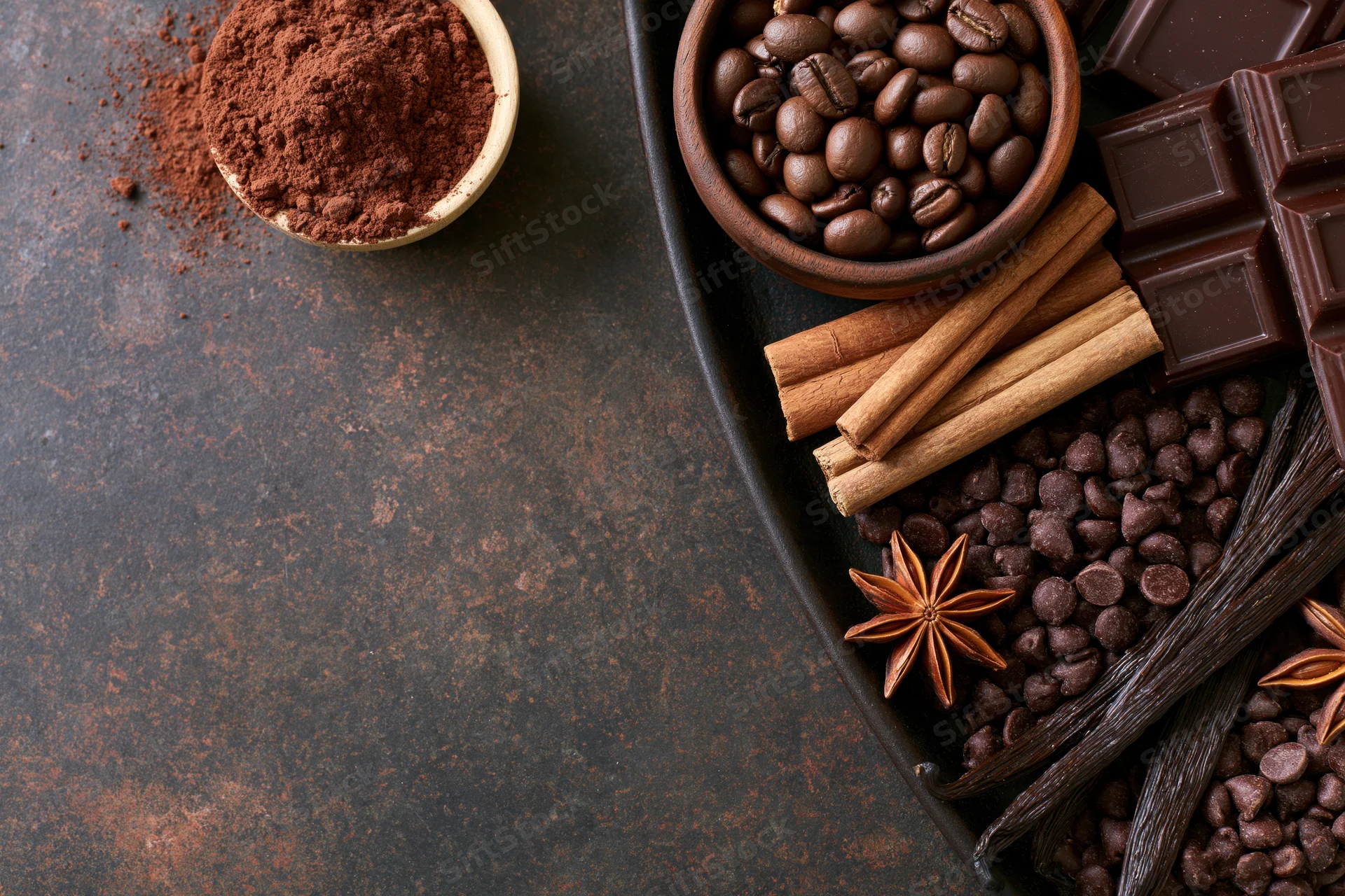 Chocolate bars, cocoa powder, coffee beans, cinnamon sticks, vanilla pods, and star anise arranged on a dark tray with copyspace on the left