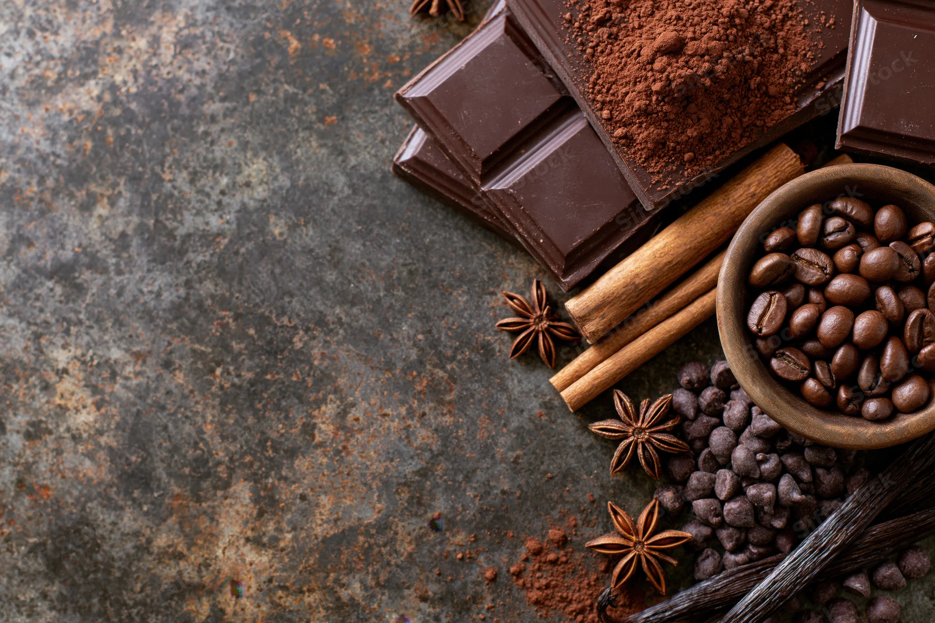 Chocolate bars, cocoa powder, coffee beans, cinnamon sticks, star anise, and vanilla pods arranged on a rustic metal surface in a flat lay composition