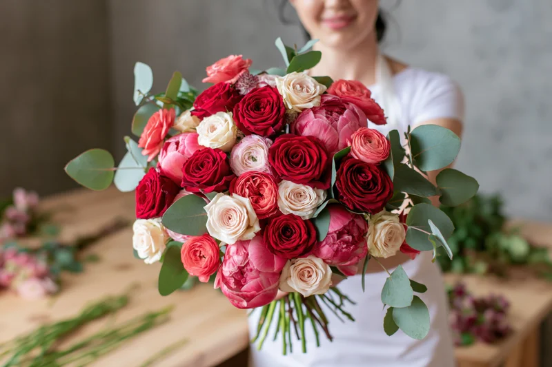 Woman holding a large bouquet of red and pink roses with eucalyptus leaves in a studio workspace