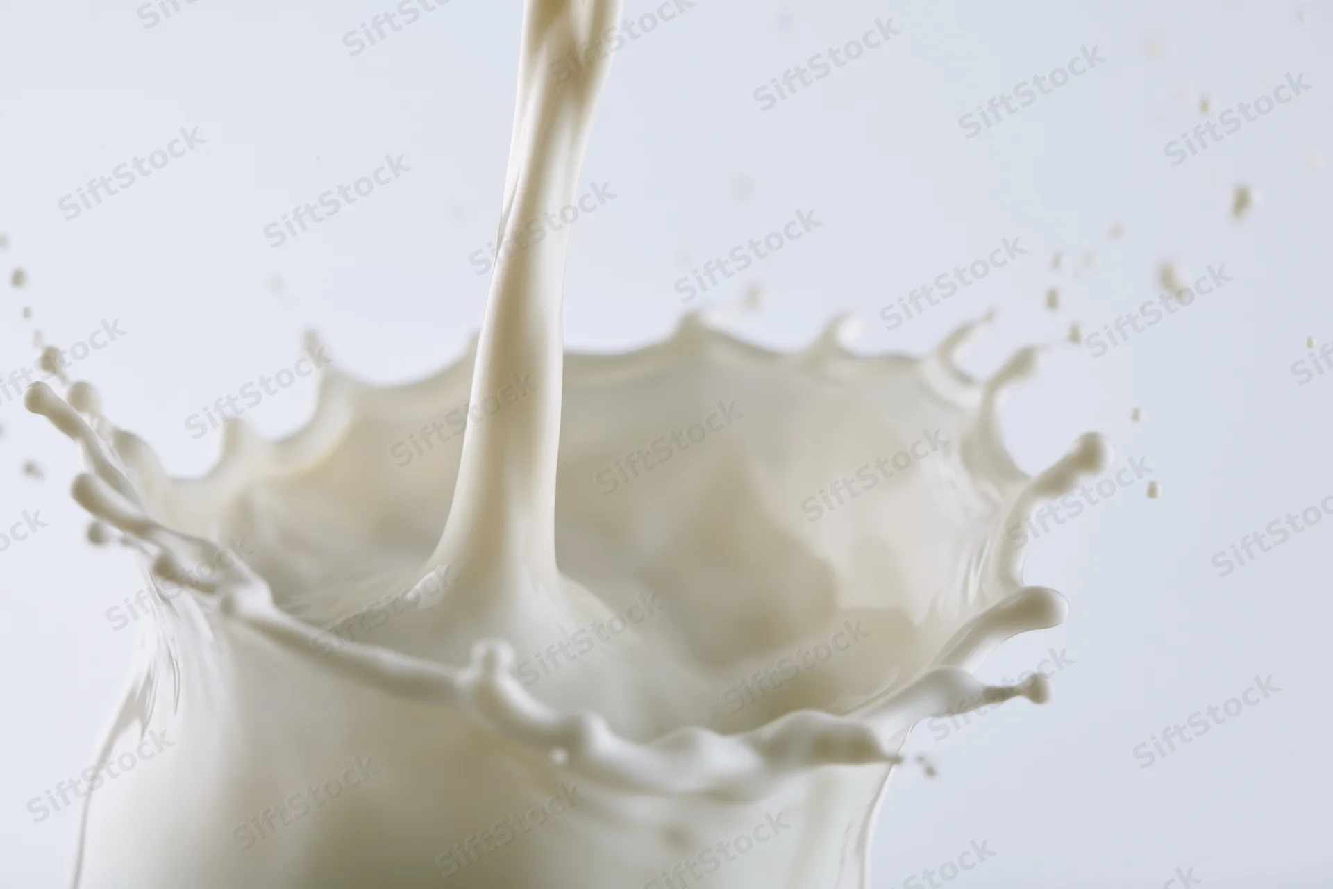 Milk splashing mid-air as a stream pours into a container against a white background