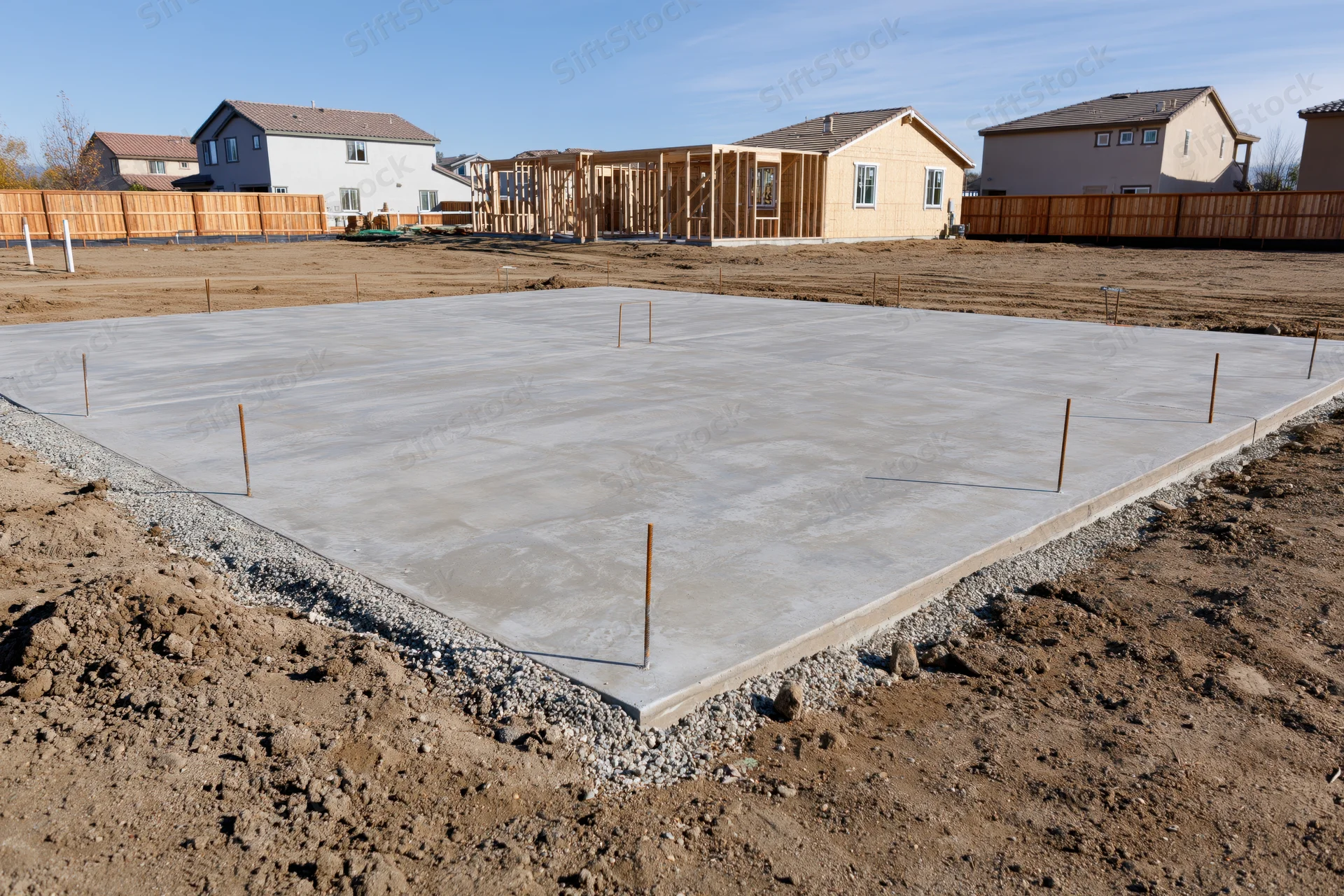 Freshly poured concrete foundation slab with rebar anchors on a residential construction site