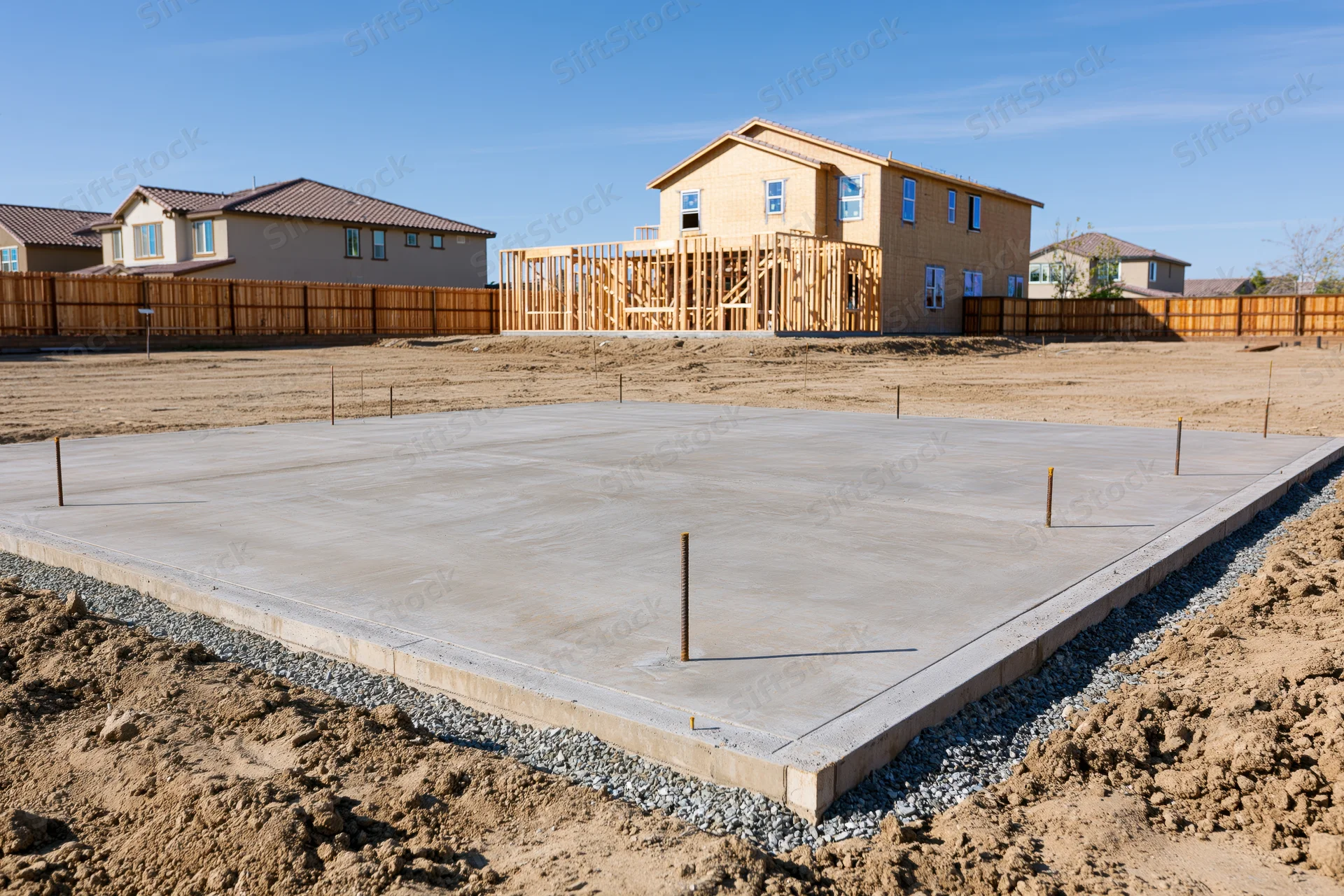 Freshly poured concrete foundation slab with rebar anchors at a residential construction site