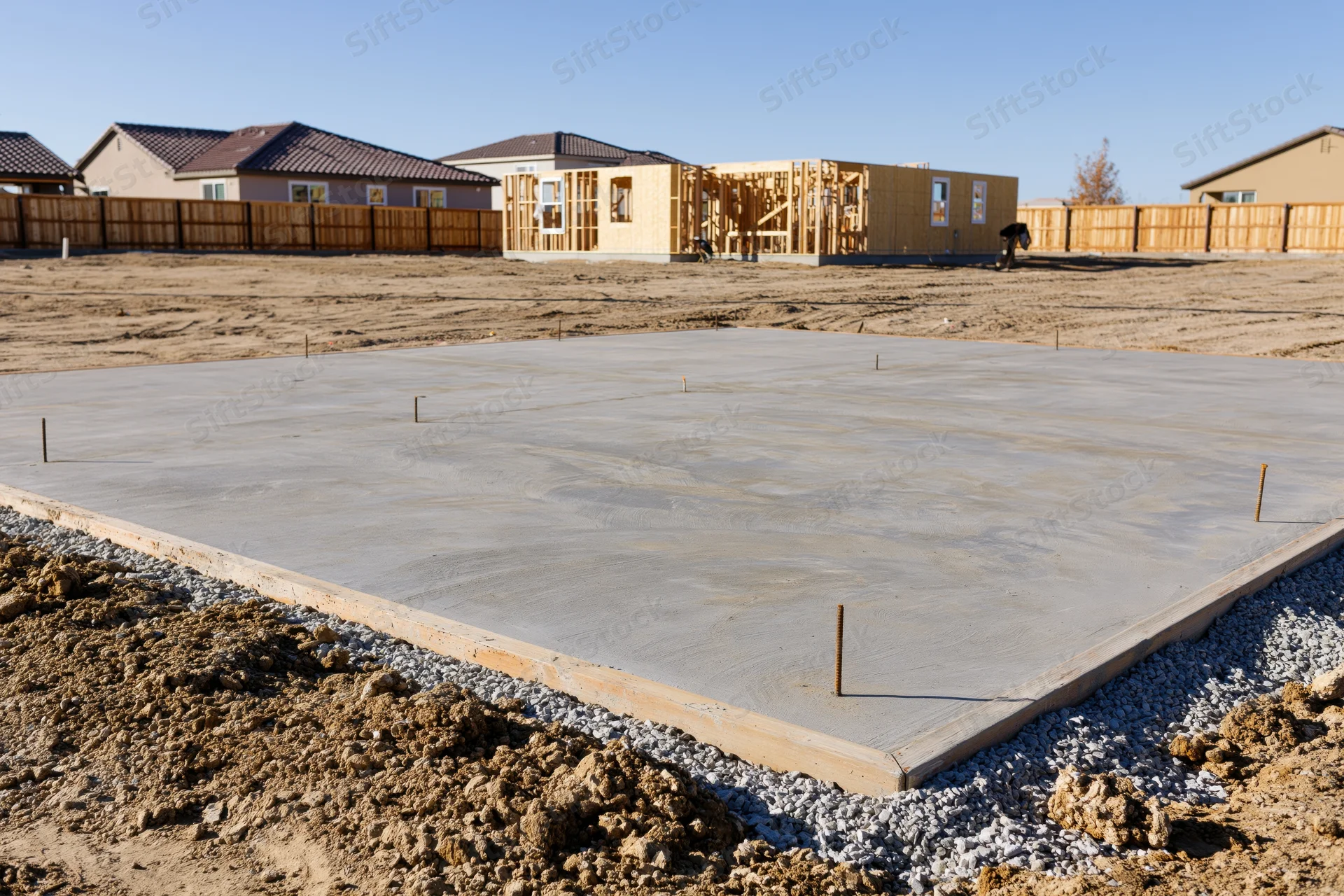 Freshly poured concrete foundation slab with rebar anchors at a residential construction site