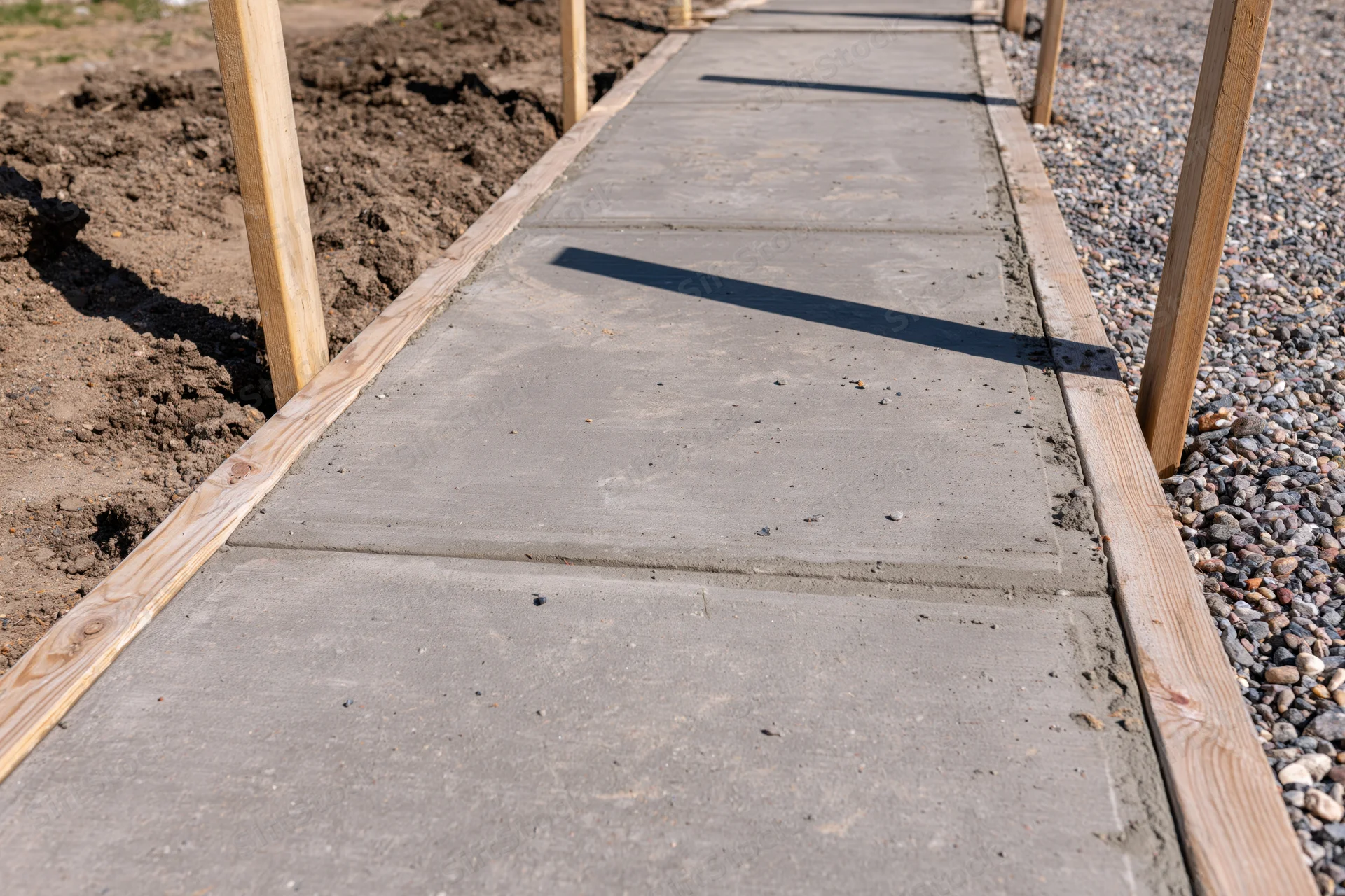 Freshly poured concrete sidewalk panels framed by wooden formwork on a construction site