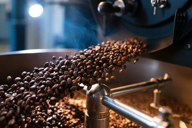 Freshly roasted coffee beans cascading from a roasting machine in an industrial setting