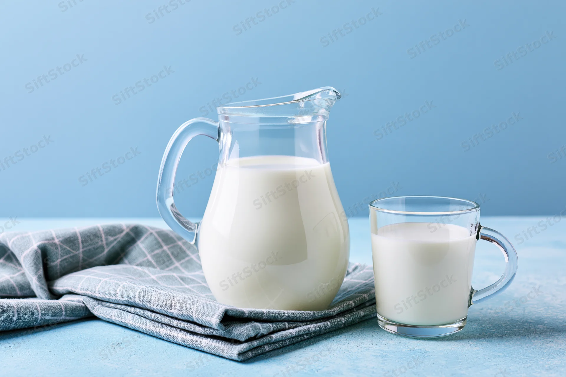 Glass pitcher and mug filled with milk on a blue surface beside a folded cloth