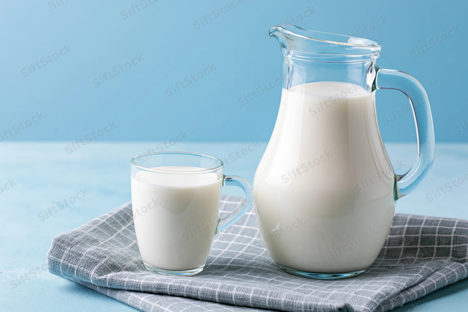 Glass pitcher and mug filled with milk on a checkered cloth over a blue surface