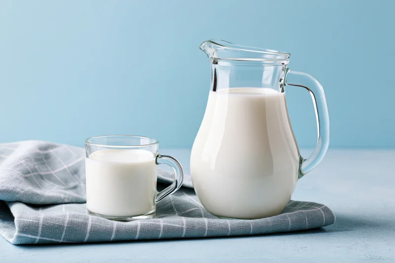 Glass pitcher and mug filled with milk on a blue surface with a checkered cloth