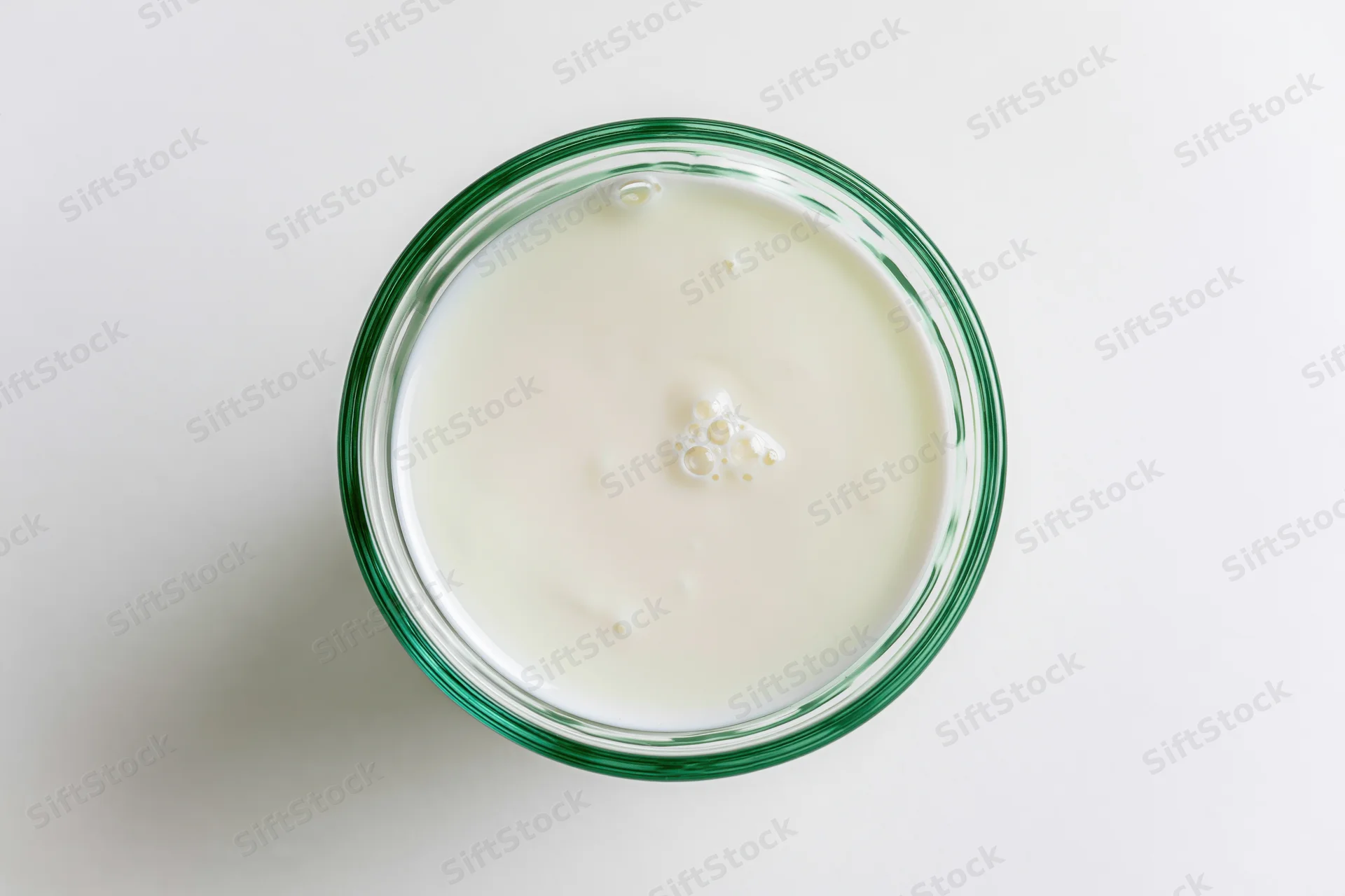 Overhead view of a glass jar filled with white yogurt on a plain white surface