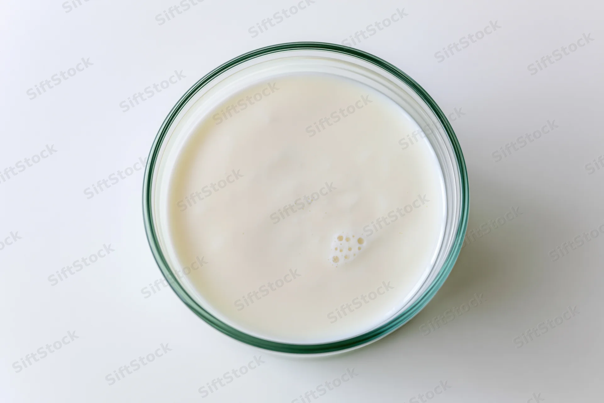 Overhead view of a glass jar filled with plain white yogurt on a white surface