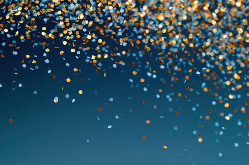 Gold and light blue confetti pieces falling densely against a dark blue background