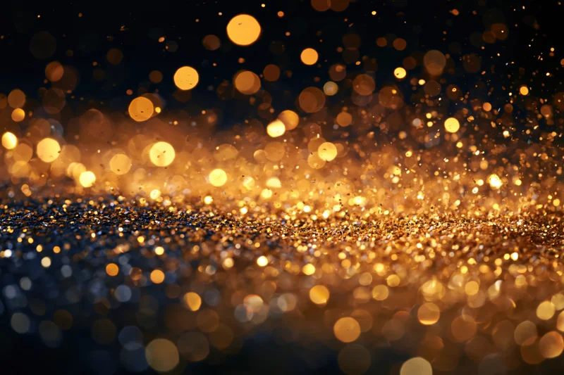 Golden glitter and light particles suspended mid-air against a dark background with bokeh effect