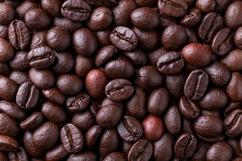 Closeup of dark roasted coffee beans filling the frame with a few lighter beans scattered throughout