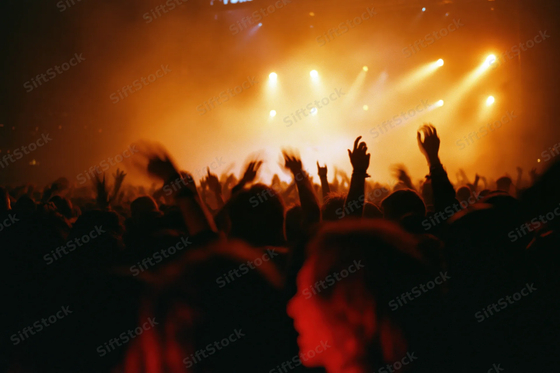 Crowd of concertgoers with hands raised toward stage lights at live music event