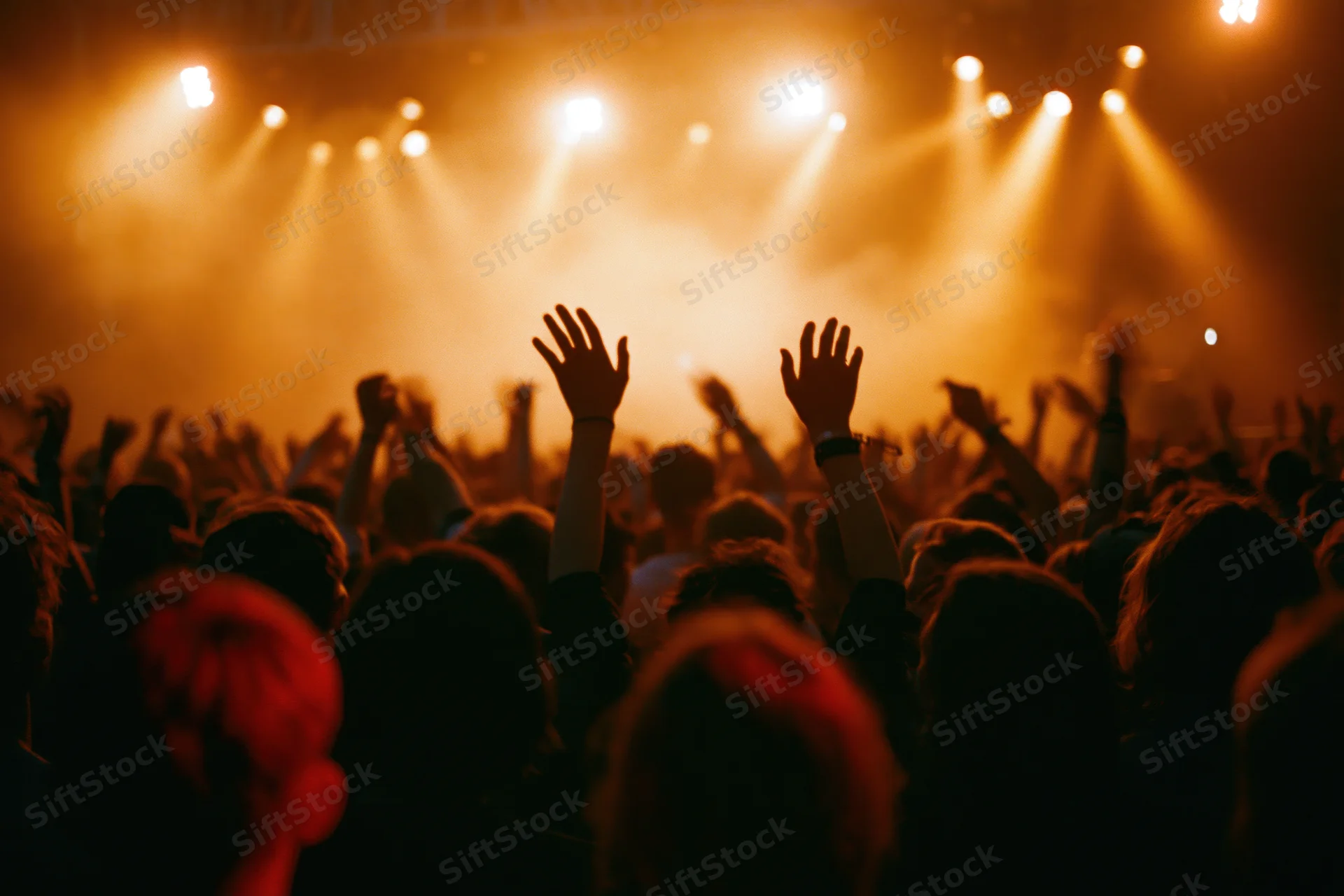 Crowd of concertgoers with hands raised toward stage lights at a live music event