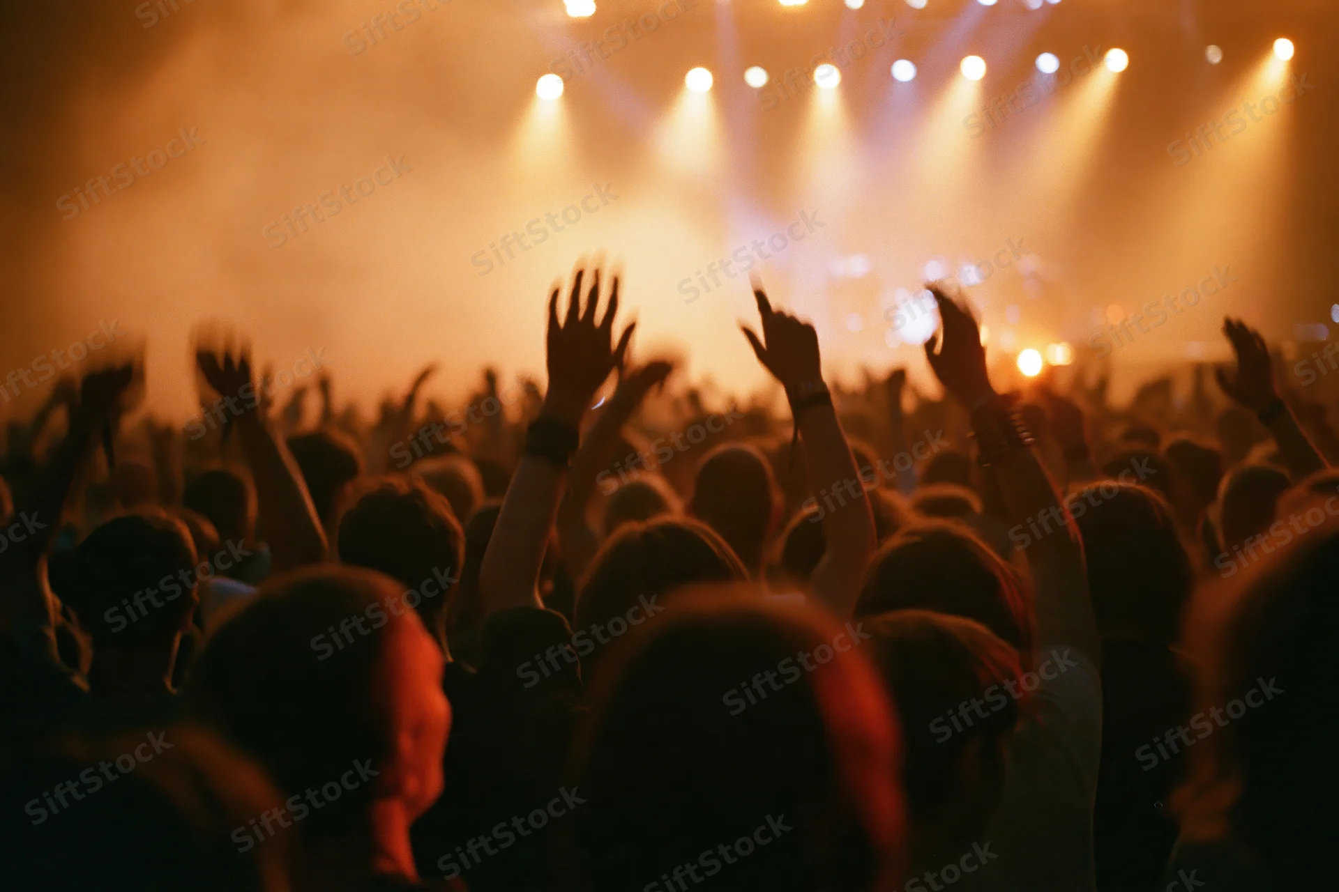 Crowd of people with hands raised at a concert under stage lights