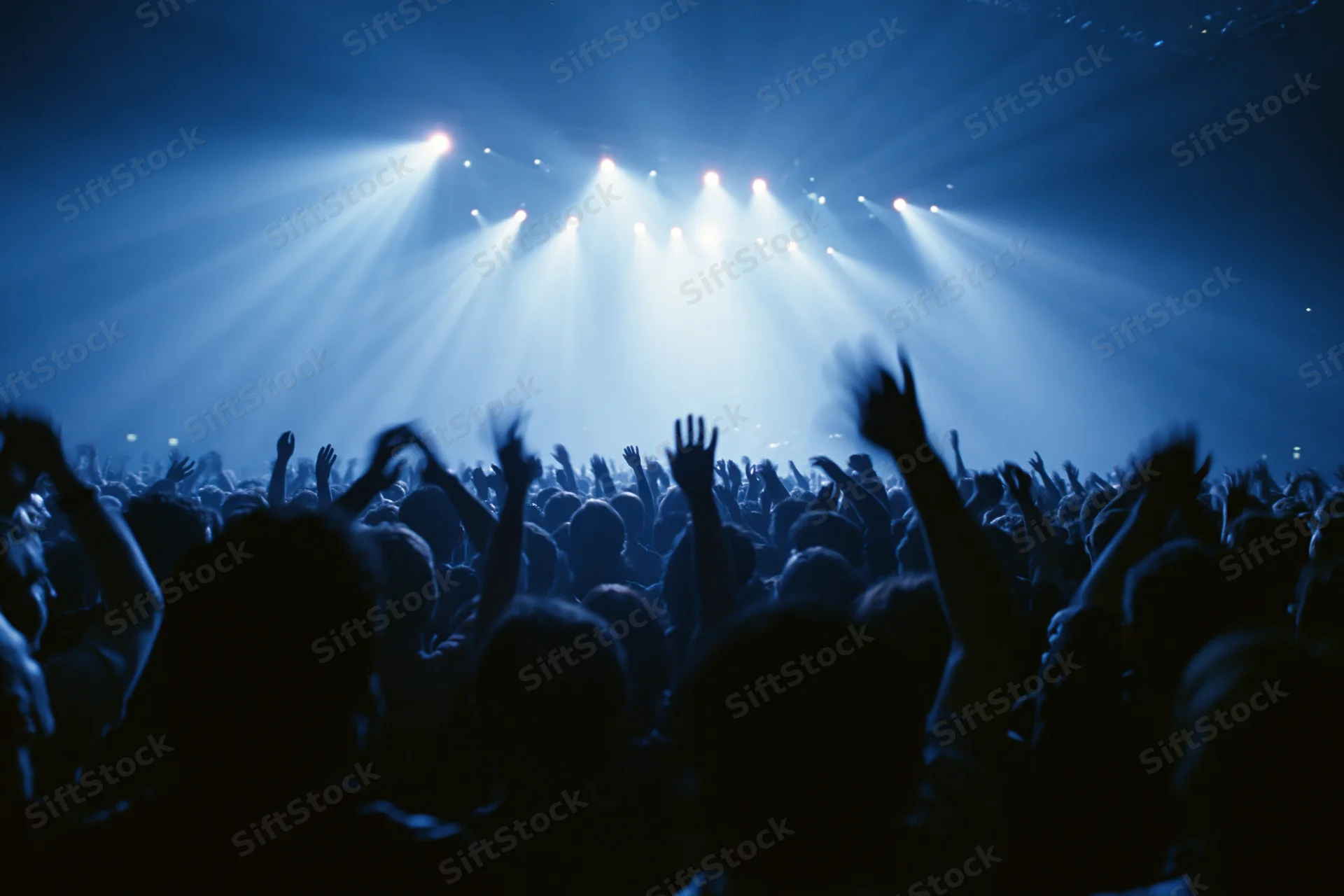 Silhouetted crowd with hands raised toward bright stage lights at concert