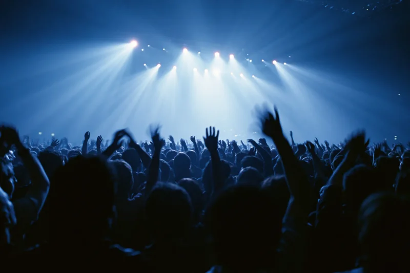 Silhouetted crowd with hands raised toward bright stage lights at concert
