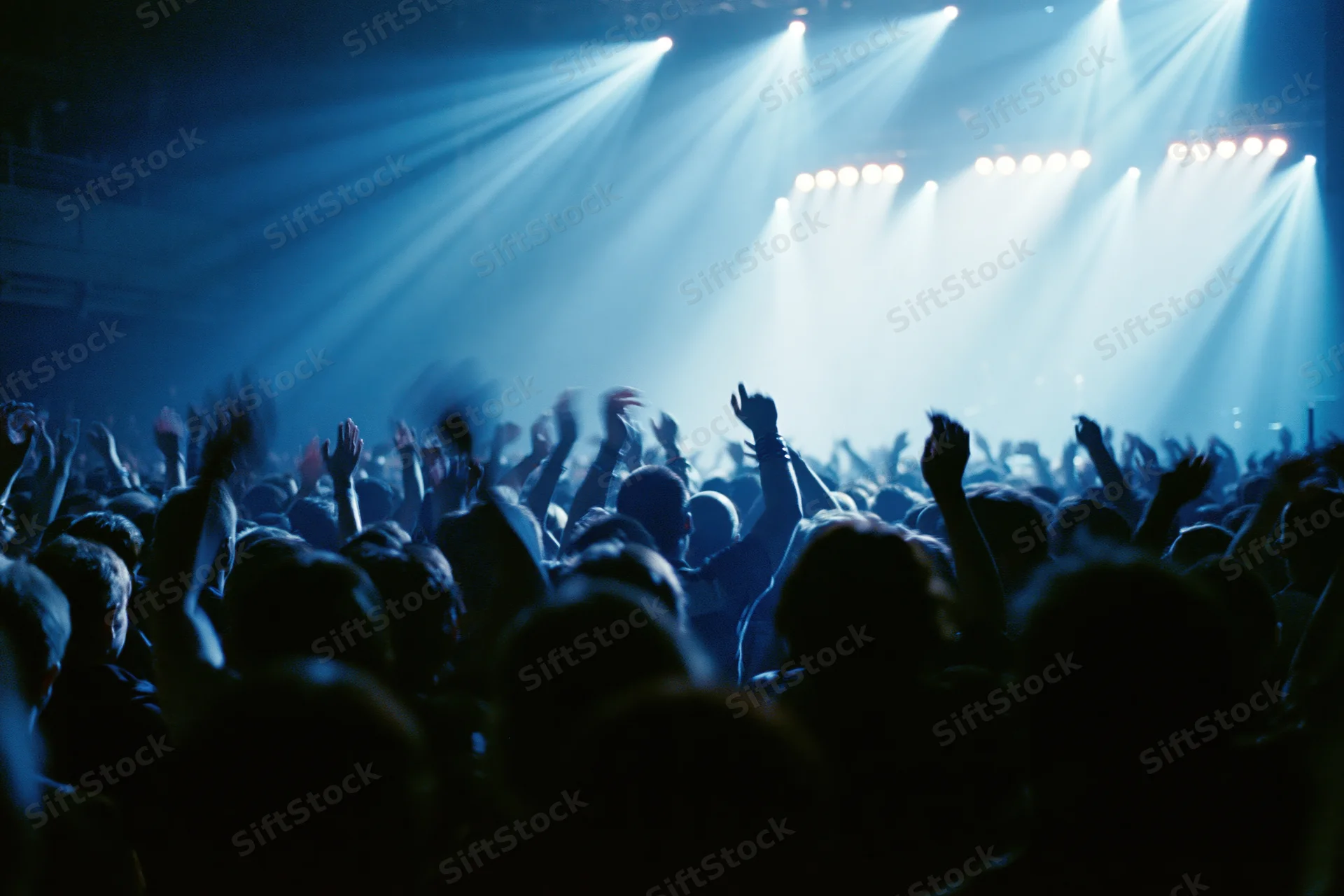 Silhouetted crowd with hands raised toward bright stage lights at concert