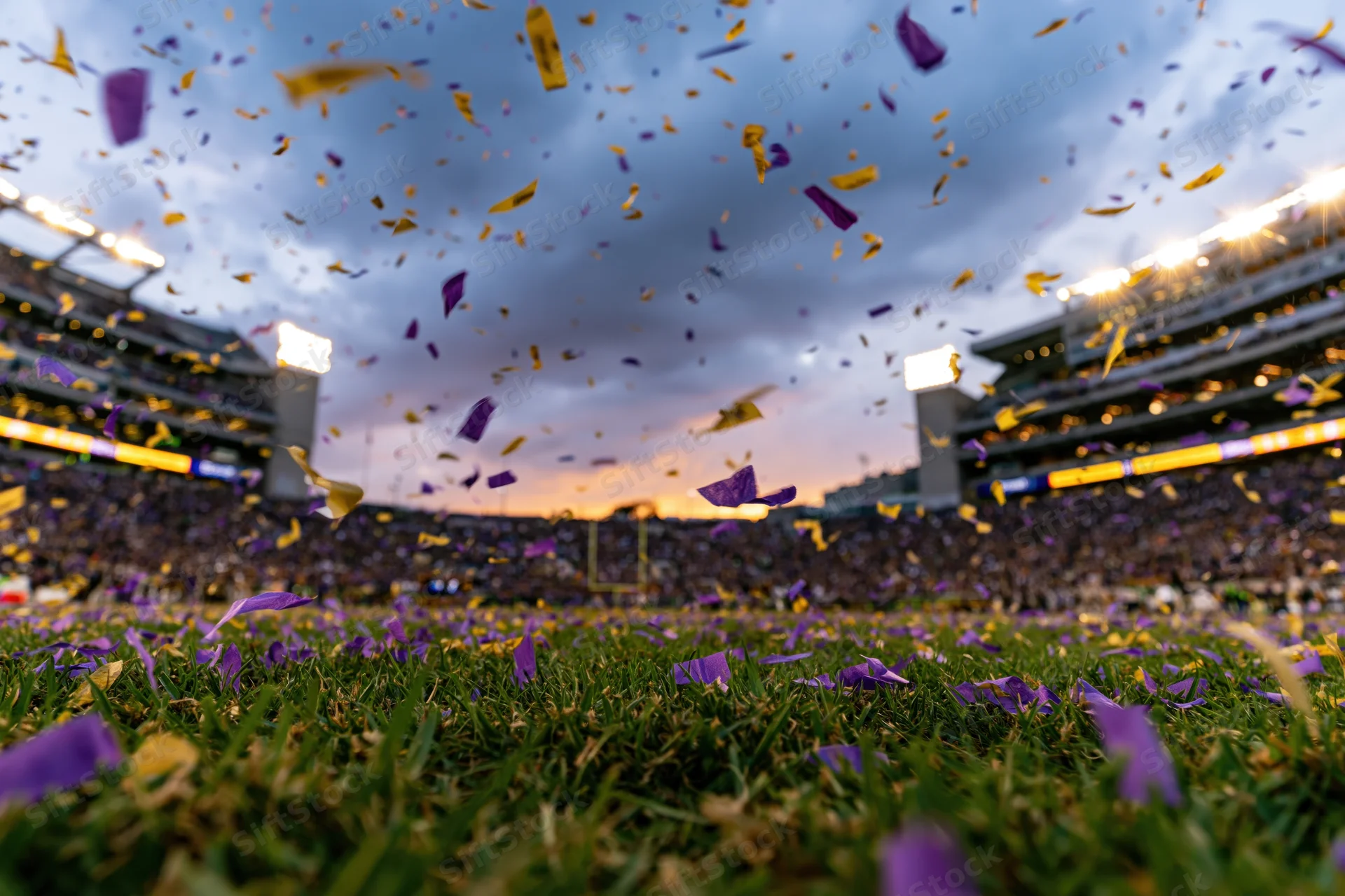 Confetti falling over a football field at sunset in a packed stadium