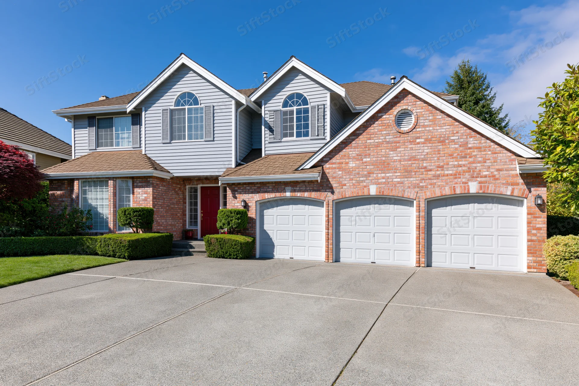 Two-story suburban house with brick and grey siding, red front door, three garages, and landscaped front yard