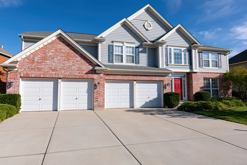 Two-story suburban house with brick and grey siding, red front door, four garages, and concrete driveway