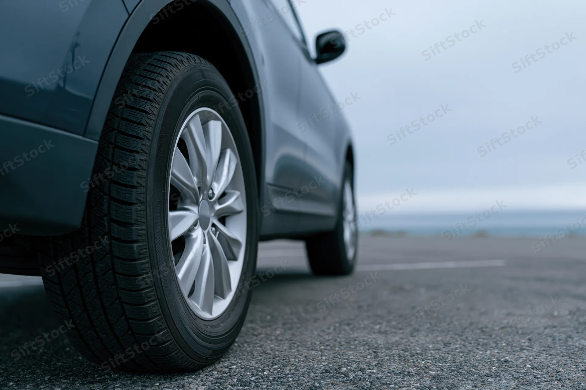 Low-angle close-up of a dark grey suv's front wheel and tire on asphalt road