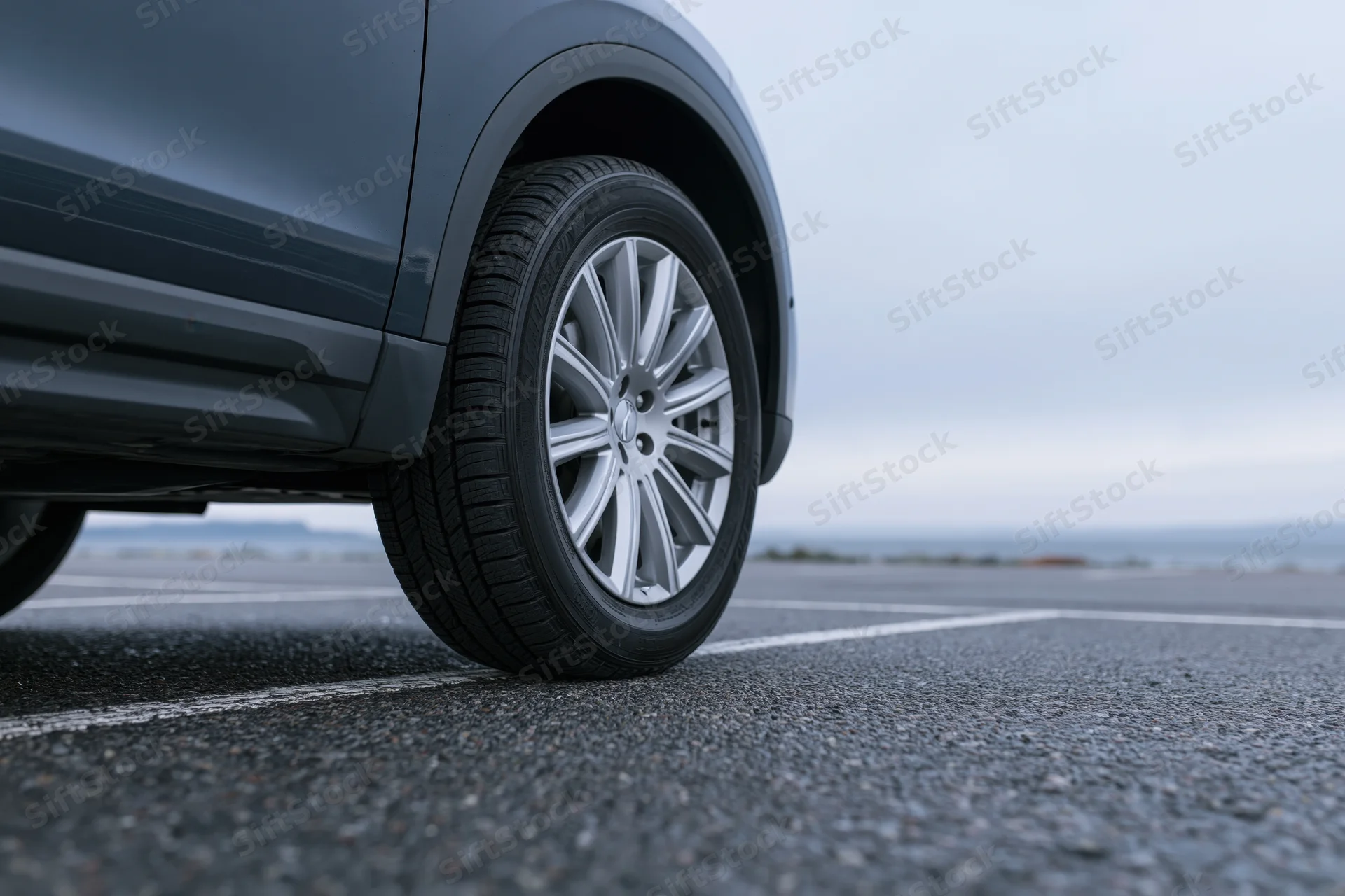 Low-angle close-up of a dark grey suv's front wheel and tire on asphalt parking lot
