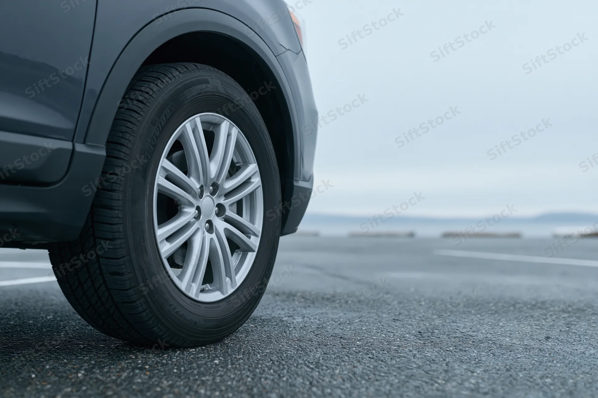Low-angle close-up of a dark grey suv's front wheel and tire on an asphalt road