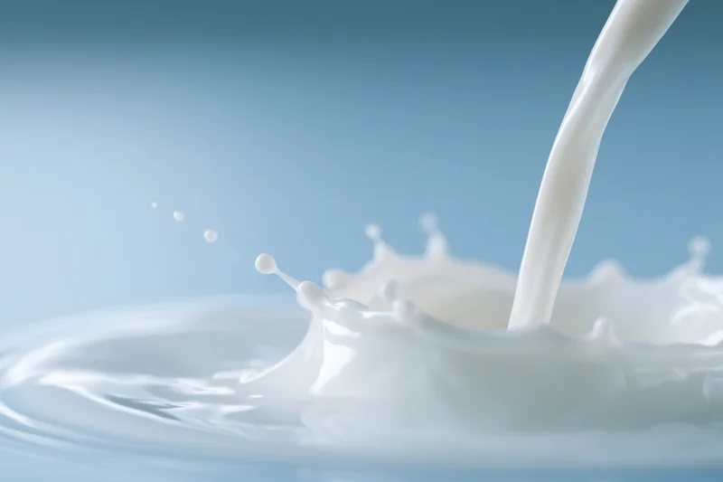 Milk being poured into a shallow pool creating a splash crown against a blue gradient background