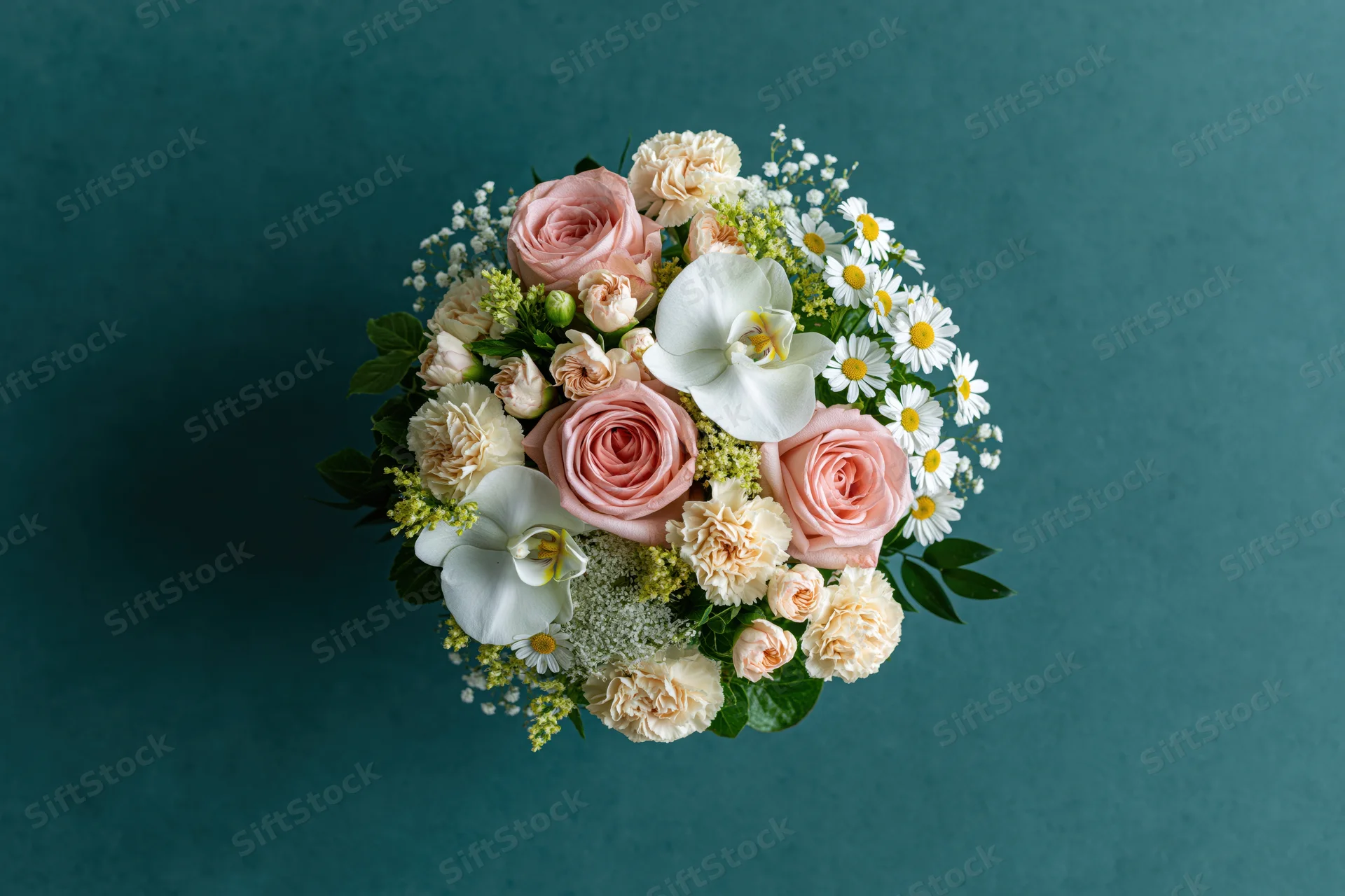Overhead view of a mixed flower bouquet with pink roses, white orchids and daisies on a teal background