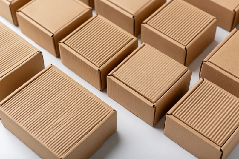 Multiple closed kraft cardboard shipping boxes arranged in rows on a white surface