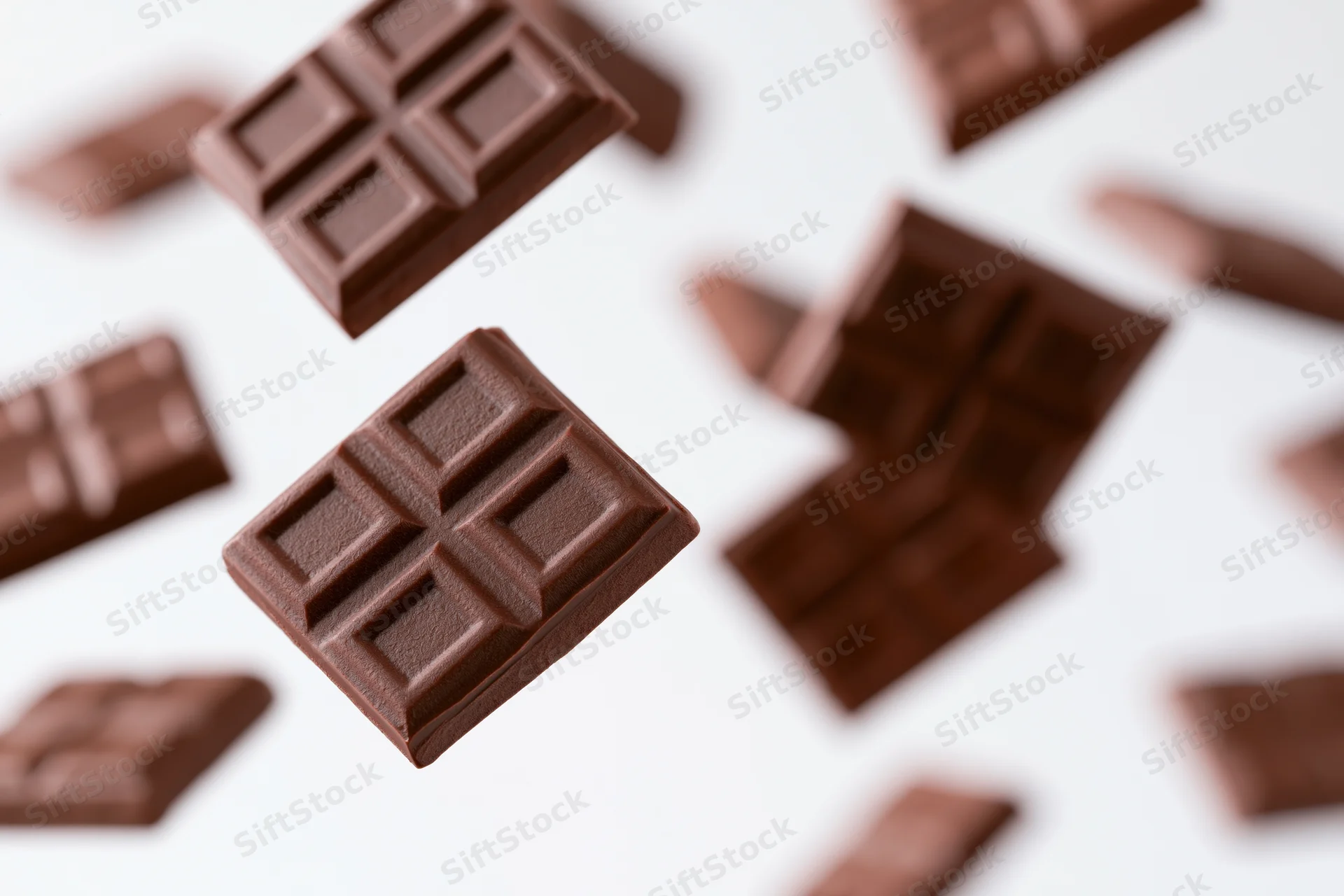 Dark milk chocolate squares tumbling in midair against a white background