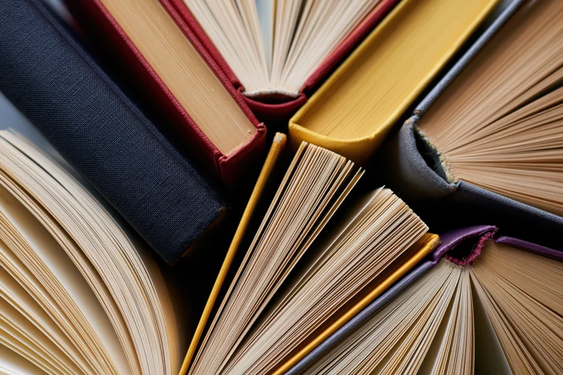 Multiple hardcover books fanned open in a stack, showing spines and pages