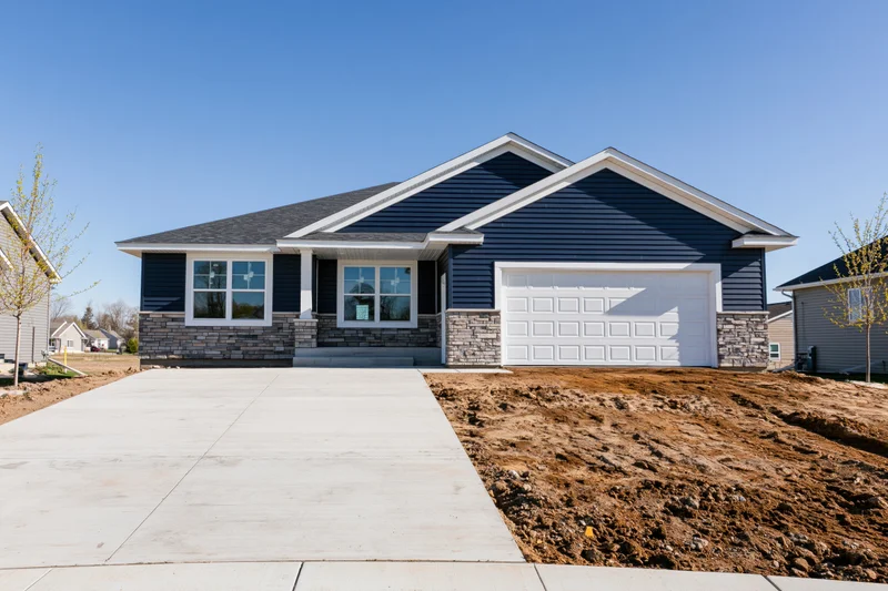 Newly built single-story ranch house with navy blue vinyl siding and stone accents on a suburban lot