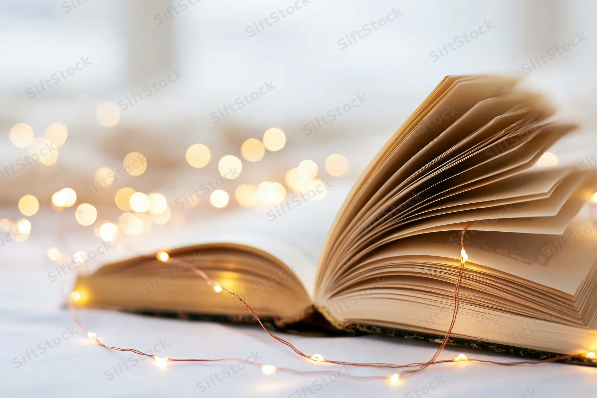 Open hardcover book with fanned pages and string lights on a white surface
