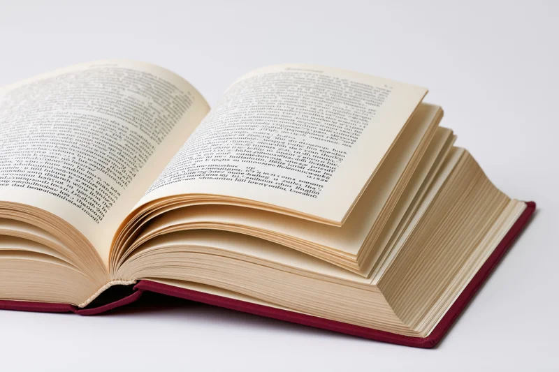 Open hardcover book with red binding lying flat pages fanned on white surface