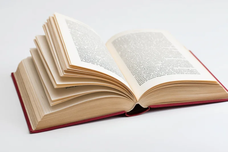 Open hardcover book with red binding lying flat and pages fanned on white surface