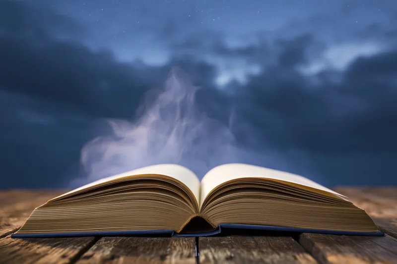 Open hardcover book with smoke rising from pages on a wooden table under a starry night sky