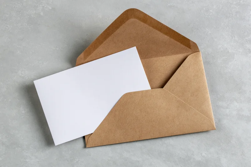 Open kraft paper envelope with blank white card on gray surface