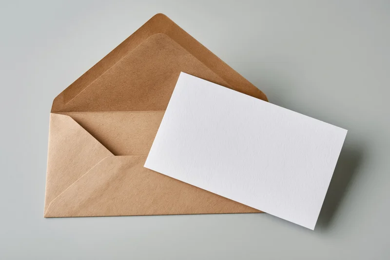 Open kraft paper envelope with blank white card resting inside, flat lay on light gray surface