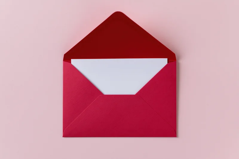Open red paper envelope with blank white card inside on pink background