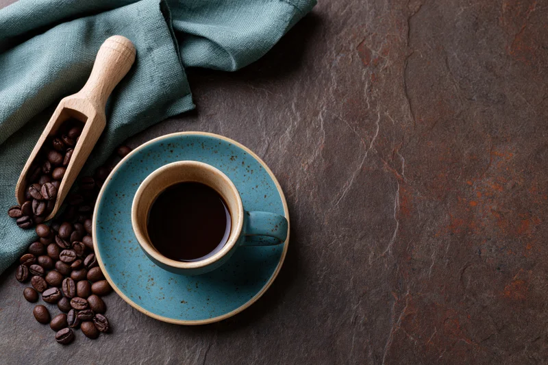Teal ceramic coffee cup with saucer and coffee beans on slate surface, overhead flat lay arrangement