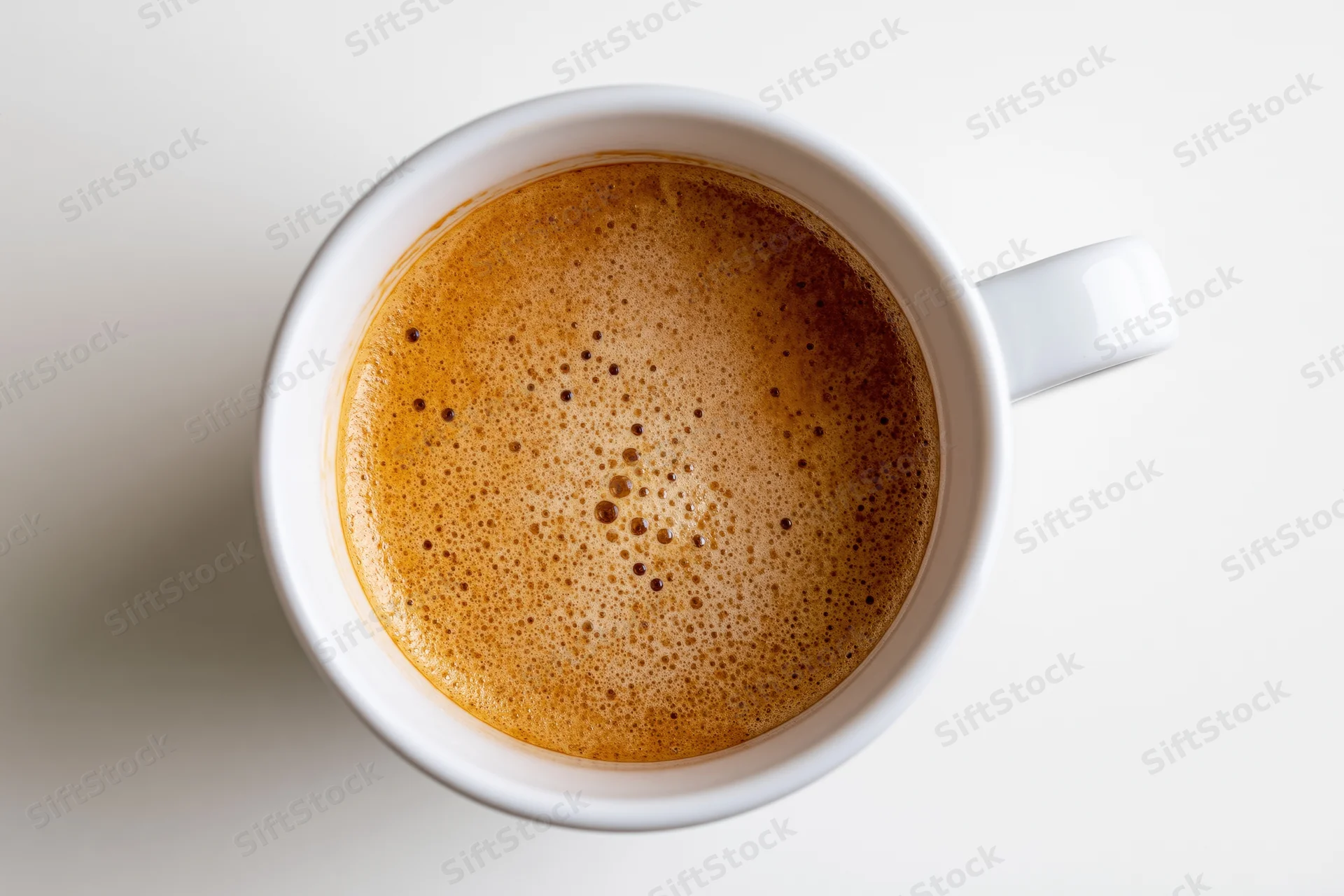 Overhead view of a white ceramic coffee cup filled with foamy espresso on a plain white surface