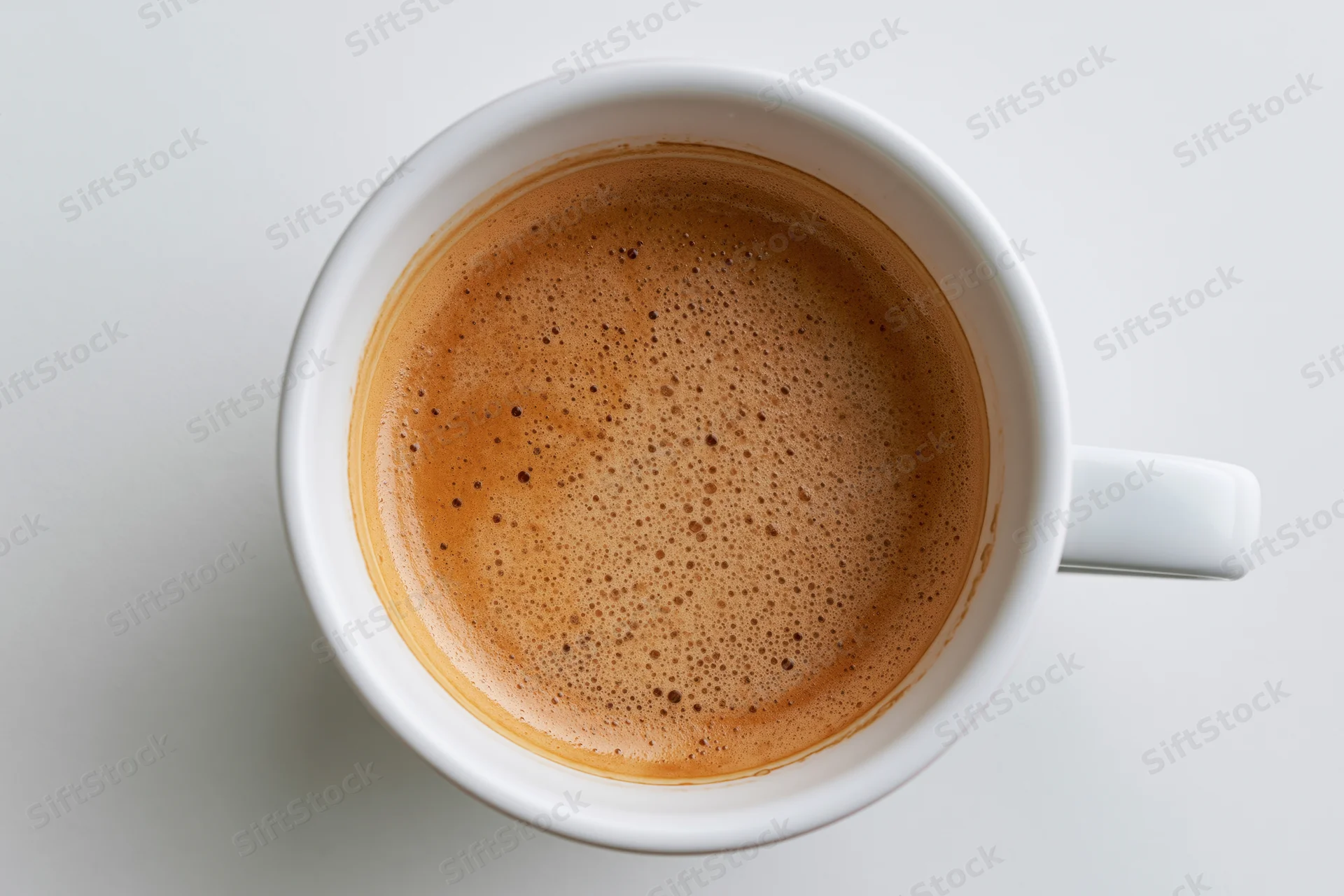 Overhead view of a white ceramic coffee cup filled with foamy coffee on a plain white surface