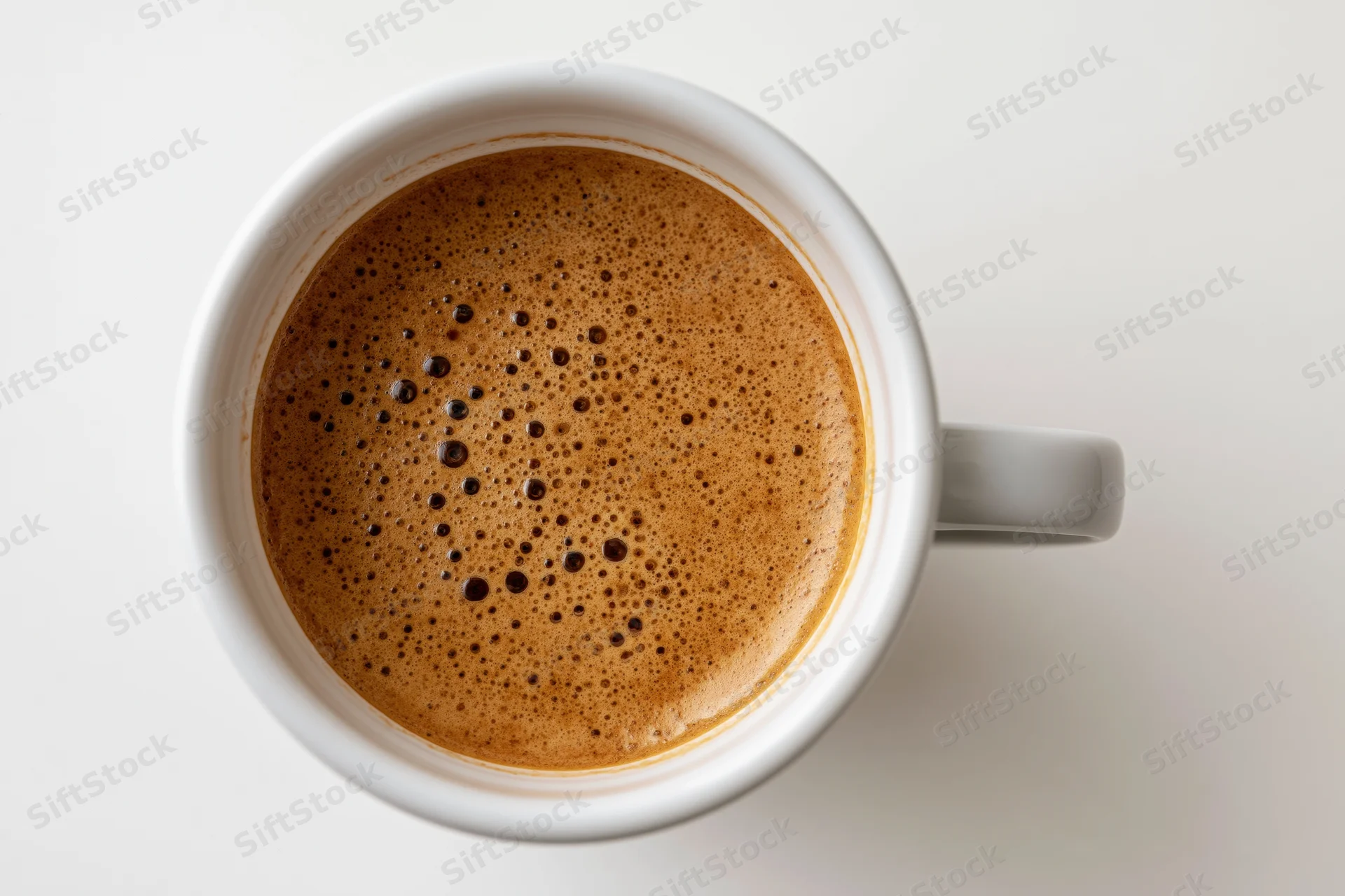 Overhead view of a white ceramic coffee cup filled with foamy espresso on a plain white surface