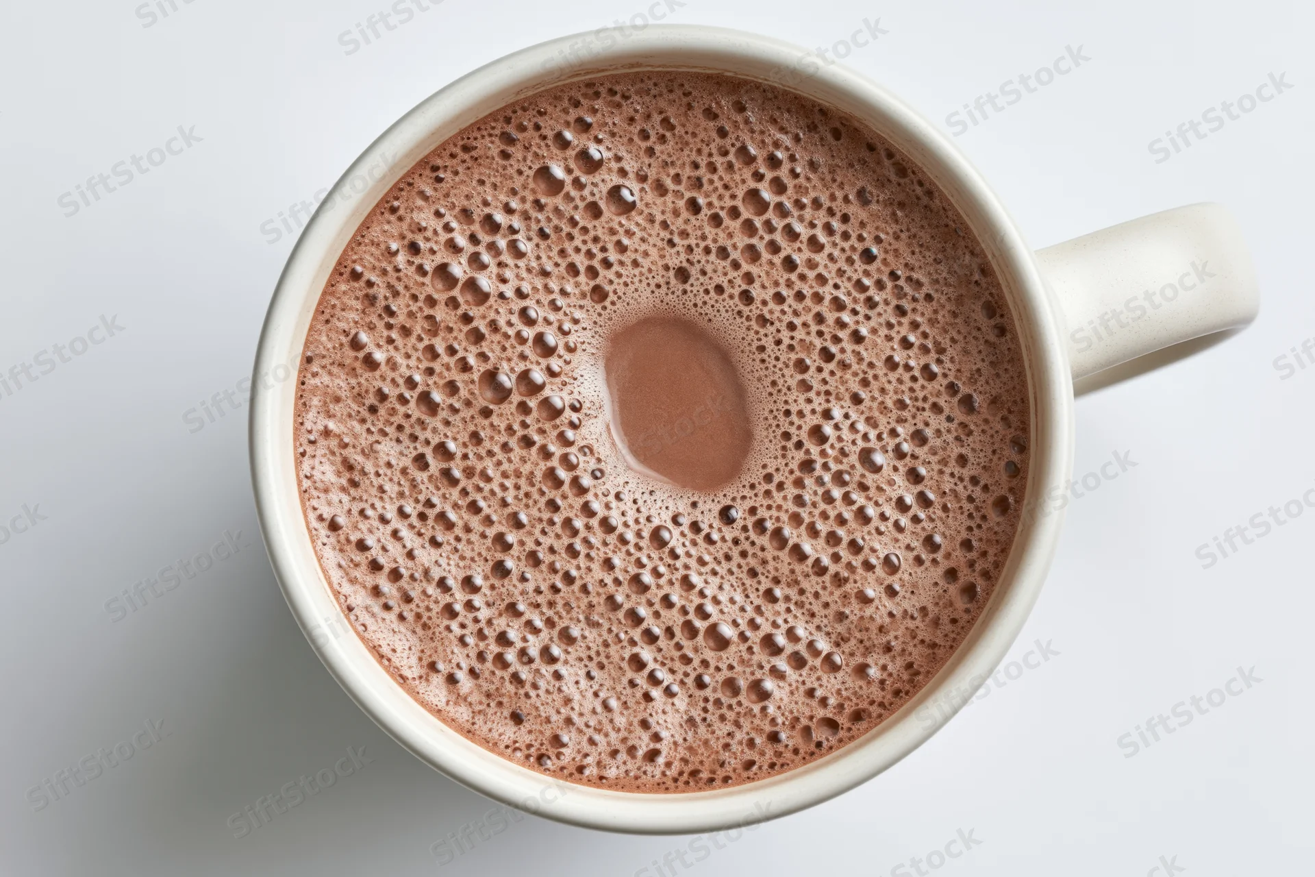 Overhead view of a white ceramic mug filled with frothy hot chocolate on a plain white surface