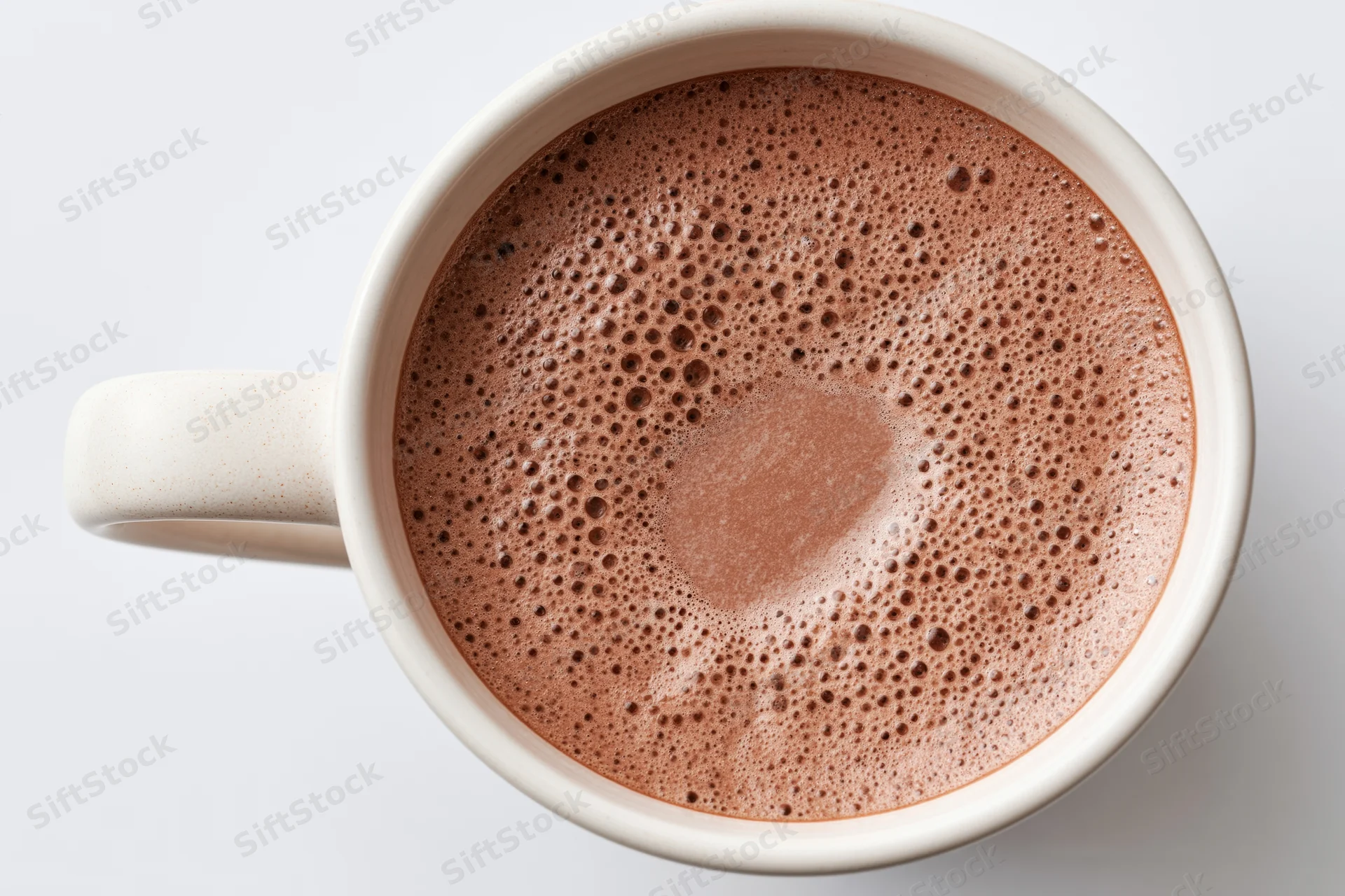 Overhead view of a white ceramic mug filled with frothy hot chocolate on a plain white surface