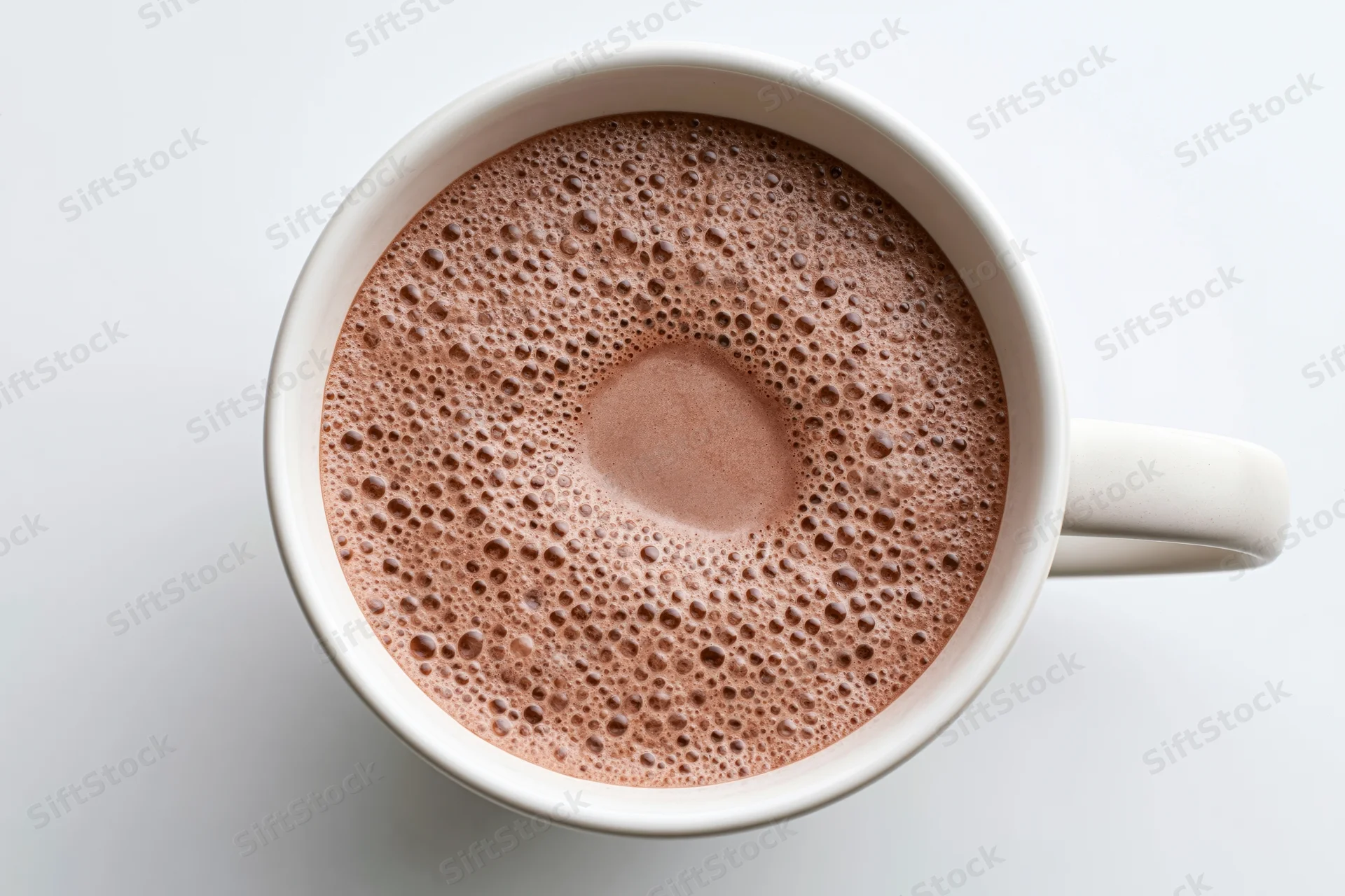 Overhead view of a white ceramic mug filled with frothy hot chocolate on a plain white surface